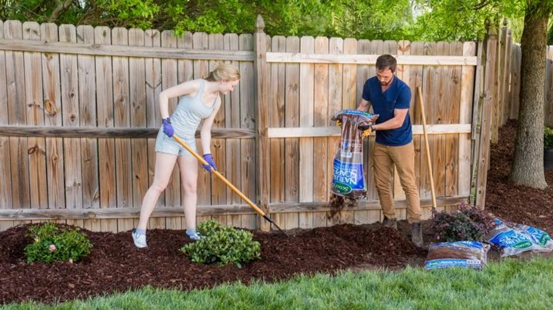 Couple spreading mulch along fence